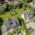 Aerial view of several houses with green lawns and parked cars.