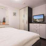 Bedroom with double bed, TV, and wardrobe. Window with blinds and plants.