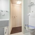 Bathroom with sink, toilet, and shower. Tiled wall and mirror visible.