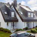 White villa with black roof and multiple windows. Front garden with flowerbeds and paved path.