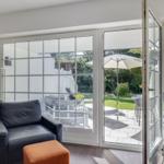 A black armchair and an orange ottoman are in front of a glass door leading to the garden.