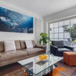 Living room with sofa, armchair, and glass table. Large window view to terrace.