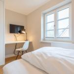Bedroom with bed, desk, TV, and window.