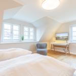 Room with two beds, desk, and windows.