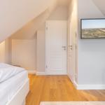 Room with two beds, wooden floor, and TV mounted on the wall.
