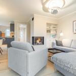 Living room with fireplace, sofa, and dining table. Kitchen in background.