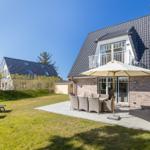 Haus mit Terrasse, Garten und Sonnenliegen unter blauem Himmel.