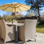 Terrasse mit Esstisch, sechs Stühlen und Sonnenschirm. Hintergrund: Grasfläche und Bäume.