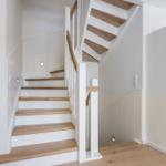 Treppenhaus mit Holzstufen und weißer Wandverkleidung.