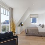 Schlafzimmer mit Dachschrägen, Balkon und Bett mit grauer Bettwäsche.