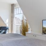 Schlafzimmer mit Blick auf Balkon und Meer. TV, Bett und Sessel sichtbar.
