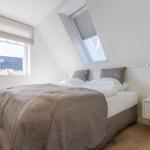 Schlafzimmer mit Dachschrägen, Bett, Nachttisch und Fenstern.