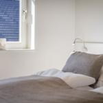Schlafzimmer mit Bett, Kopfkissen und Fenster mit dekorativer Lampe.