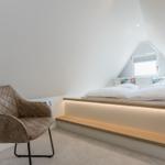 Schlafzimmer mit Dachschräge, Bett mit Holzrahmen und Sitzbank. Braune Ledermöbel.