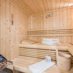 Holzsauna mit Bänken, Handtuch und Eimer. Ofen mit Steinen und Warnschild.