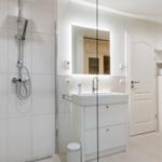 Badezimmer mit Dusche, Waschbecken und Toilette. Spiegelschrank und Holzverkleidung sichtbar.