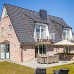 Haus mit Steinmauer, Terrasse und Gartenbereich mit Sitzgruppe.