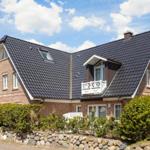 A two-story house with brick facade and dark roof. A well-kept garden is in front of the house.