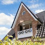 Two-story house with balcony and tiled roof under blue sky.