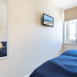 Bedroom with blue bedding, wall-mounted TV, and window with view.