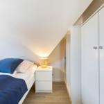 Bedroom with bed, nightstand, and wardrobe under sloped ceiling.