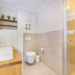 Bathroom with shower, toilet, and sink on wooden base.
