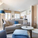 Living and kitchen area with sofa, tables, and windows.
