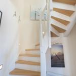 Light staircase with wooden steps and white railings. Wall pictures show pier and sea.