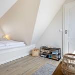 Bedroom with sloped ceiling, round window, bed, and wicker chair.