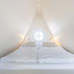 Double bed under sloped ceilings with round window and bedside lamps