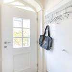 Bright entrance hall with white door and coat rack. A bag hangs on a hook.