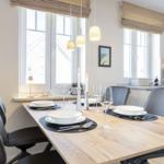 Dining area with wooden table, black chairs, and windows with blinds.