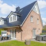 Ein zweistöckiges Haus mit rotem Backstein und dunklem Dach. Außenbereich mit Gartenmöbeln.