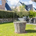 Hinterhof mit Garten, Sitzgelegenheit und Korb. Steinmauer und Hecke im Hintergrund.