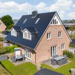Haus mit Terrasse, Garten und Grillplatz. Schwarze Dachziegel und rote Ziegelmauer.