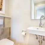 Badezimmer mit Waschbecken, Spiegel und Toilette. Wand mit Steinfliesen und Kunstwerk.