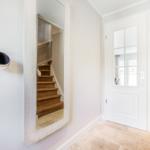 Hausflur mit Spiegel, Holztreppe und weiße Tür mit Glasfenstern.