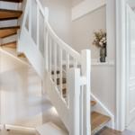 Treppenhaus mit Holzstufen und weißer Balustrade. Neben dem Flur ist ein Badezimmer sichtbar.