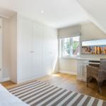 Schlafzimmer mit weißem Schrank, Schreibtisch und TV unter Dachschräge.