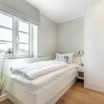 Schlafzimmer mit weißem Bett, Kleiderschrank und Fenster mit Blick auf Dächer.
