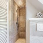 Dusche mit Steinwand, Heizkörper und WC mit Schalter.