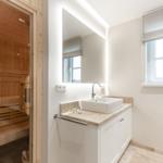 Badezimmer mit Waschbecken, Spiegel und Sauna im Hintergrund.