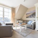 Living room with sofa, armchair, and table. Large windows and white cabinet.