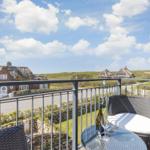 Balcony with table and chairs overlooking thatched-roof houses and green dunes.