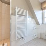 Bathroom with shower, heater, and toilet under sloped ceiling.