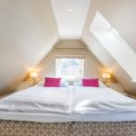 Bedroom with double bed, skylight, and window with roller blind.