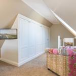 Bedroom with sloped ceiling, white closet, and patterned armchair.