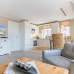 Living and kitchen area with sofa, TV, and dining table under a sloped ceiling.