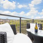 Terrasse mit zwei Sesseln, Tisch und Weinflasche. Blick auf grüne Landschaft und Haus.