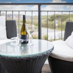 Terrasse mit Tisch, Stühlen und Weinglas. Blick auf grüne Landschaft.